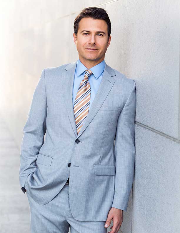 Corporate Photography of lawyer in grey suit leaning against wall outdoors. Mixture of Studio and Outdoor Lighting
